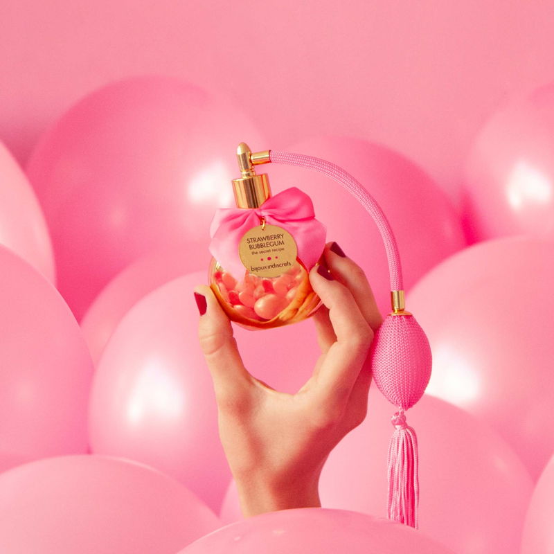 mano emerge da vasca di palloncini rosa con in mano il profumo al bubble gum bijoux indiscrets